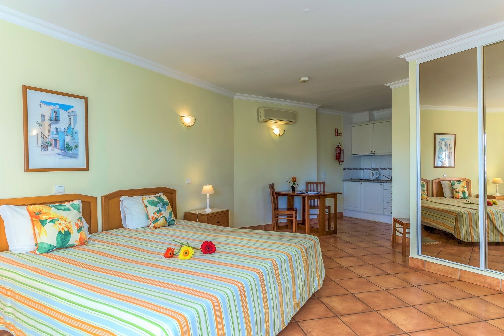 A hotel room with a bed, a small table with chairs, a kitchenette, and a bathroom with a shower.