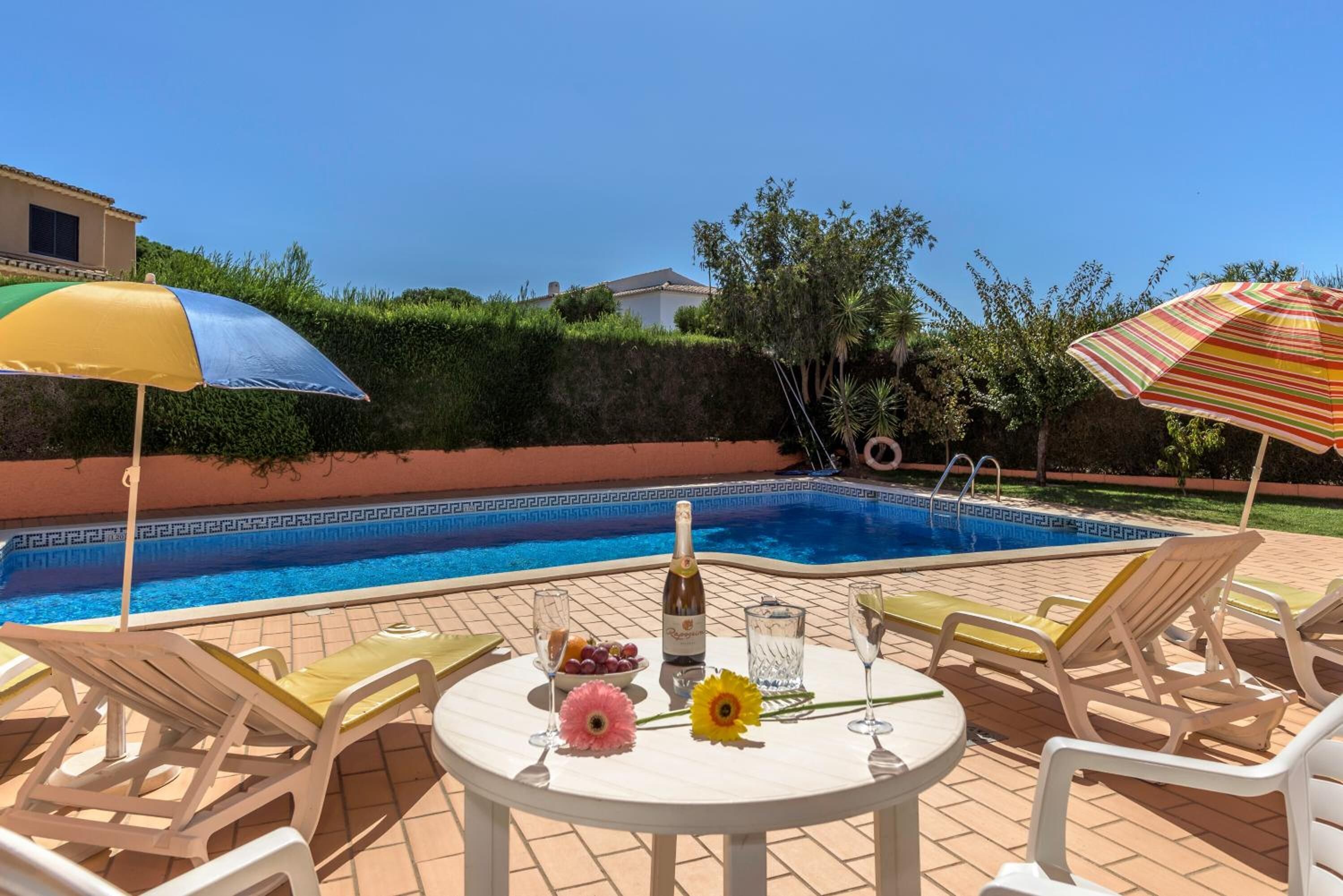 Een zwembadterras met een tafel voor twee personen, een fles champagne en een schaal fruit.