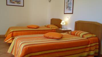 A hotel room with two beds, each with striped bedding and orange pillows. There is a nightstand with a lamp between the beds.
