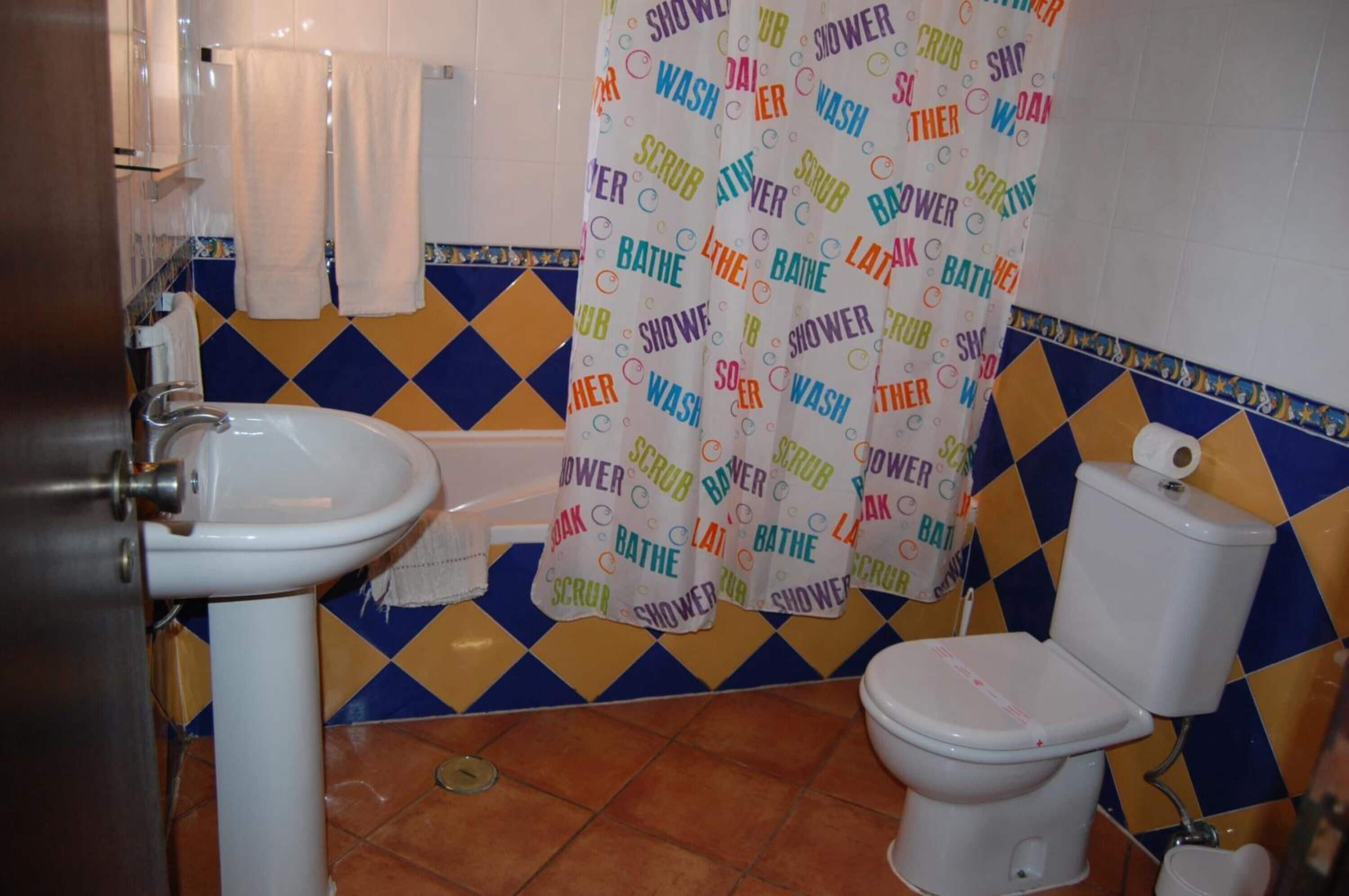 Un bagno con lavandino, wc e tenda per la doccia.