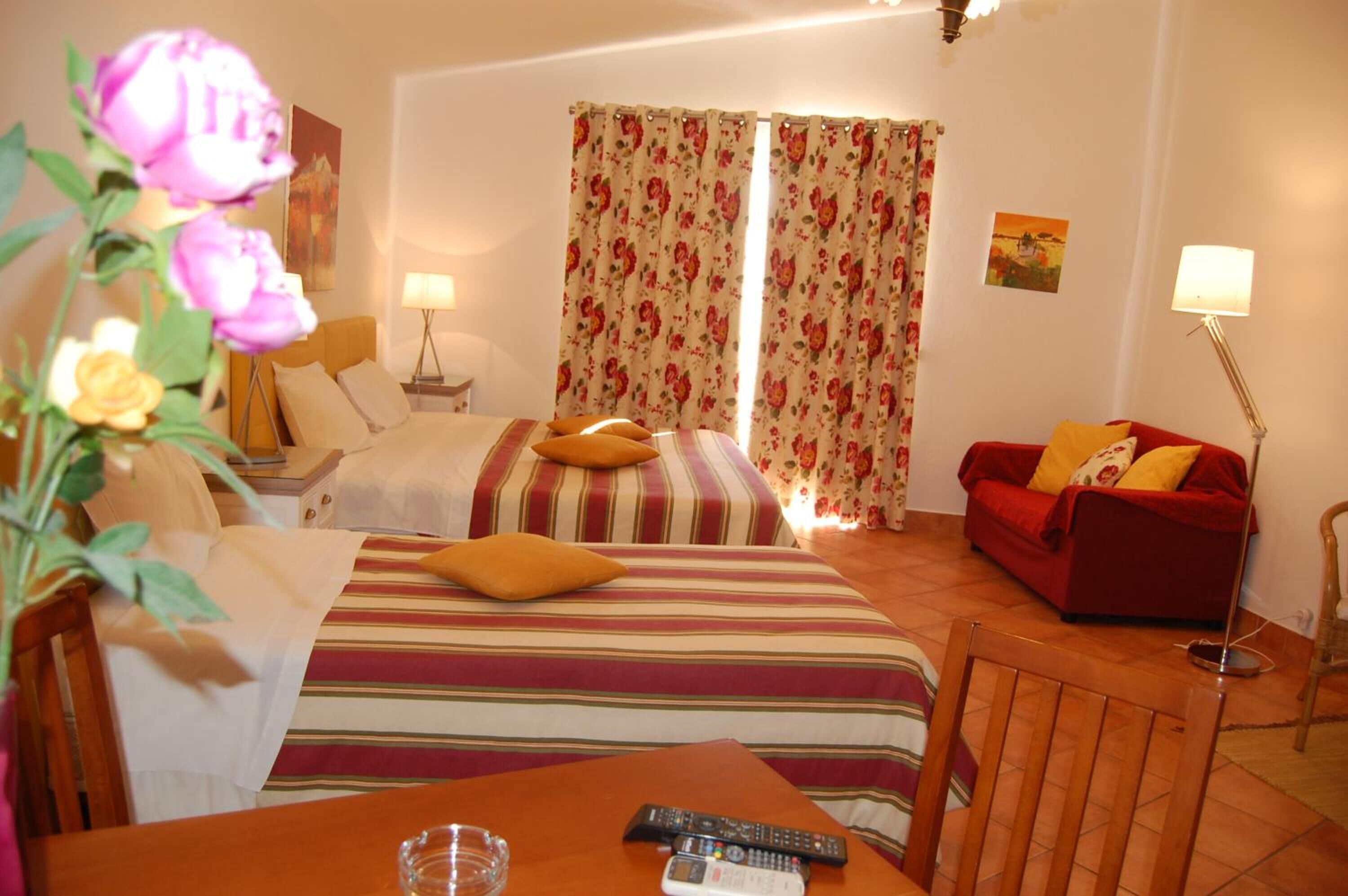Una habitación de hotel con una cama, un sofá rojo, una mesa con un control remoto y una lámpara.