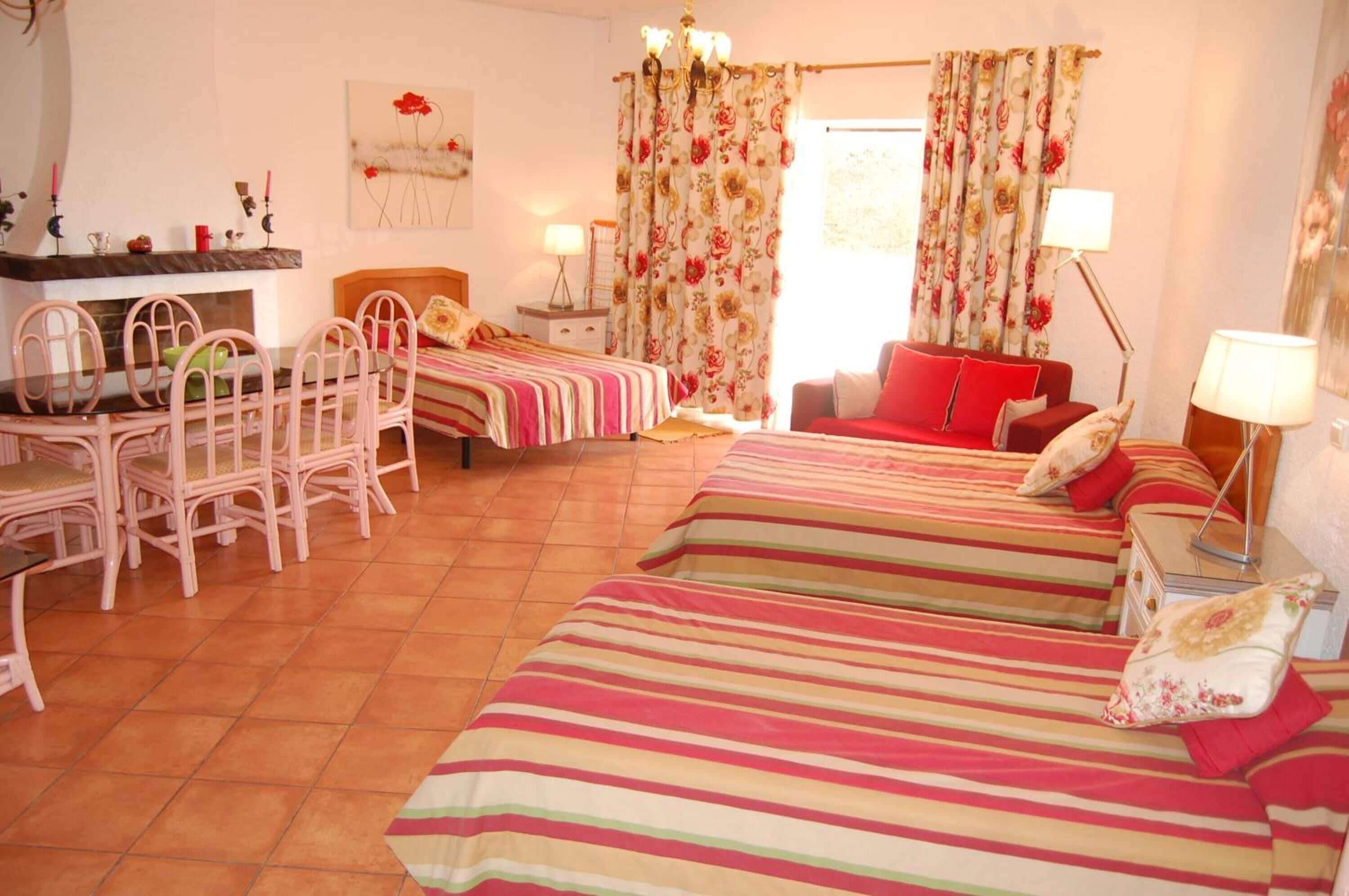 A room with two beds, a dining table with chairs, a red sofa, and a chandelier.