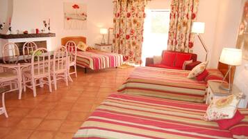 A room with two beds, a dining table with chairs, a red sofa, and a chandelier.