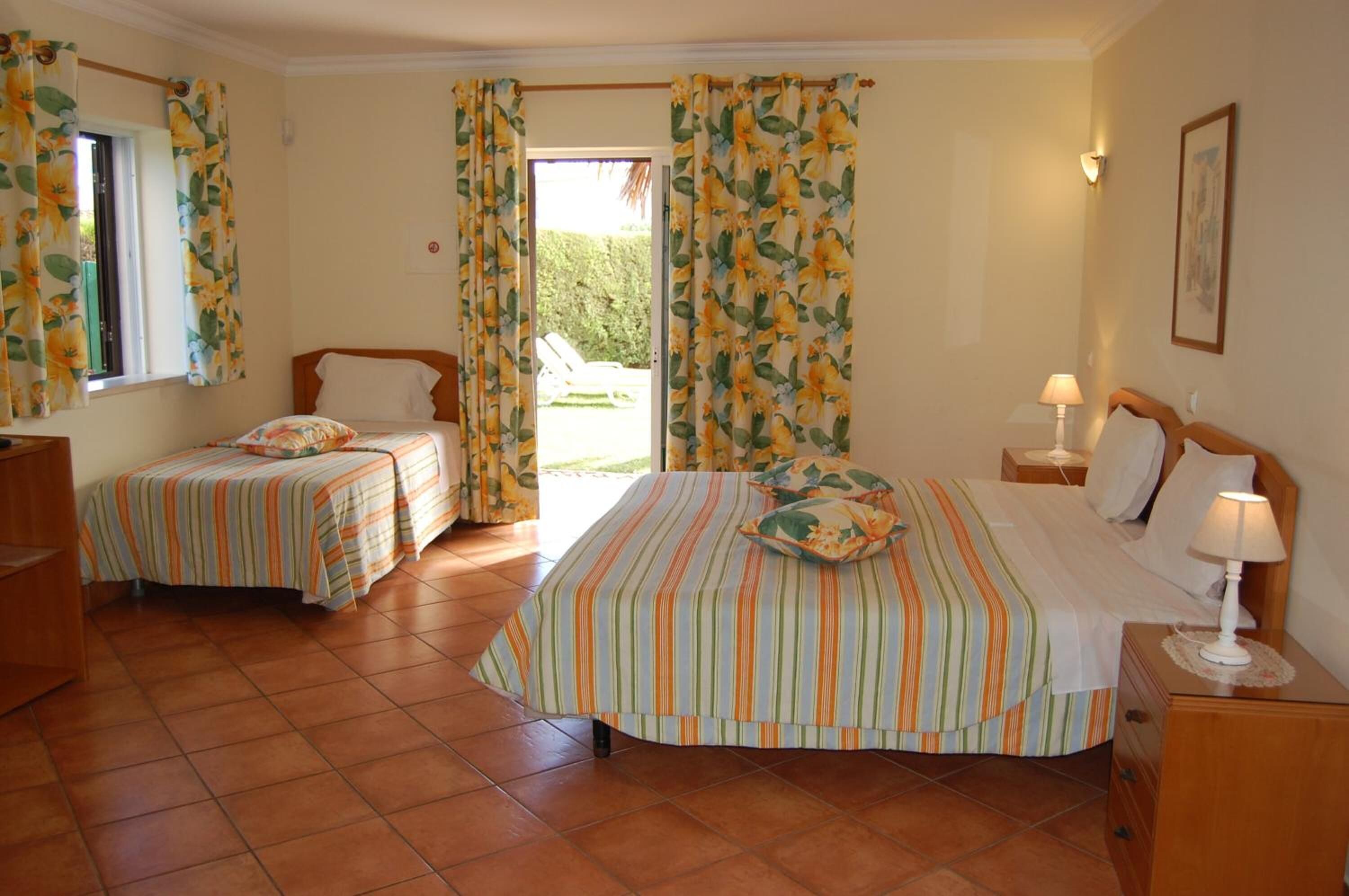 Une chambre avec deux lits simples, un lit plus grand et une fenêtre avec des rideaux.