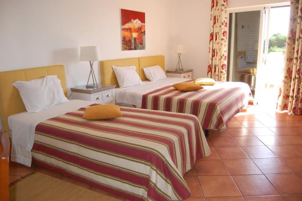 A hotel room with two beds, each with striped bedding and pillows, a nightstand with a lamp, and a painting on the wall.
