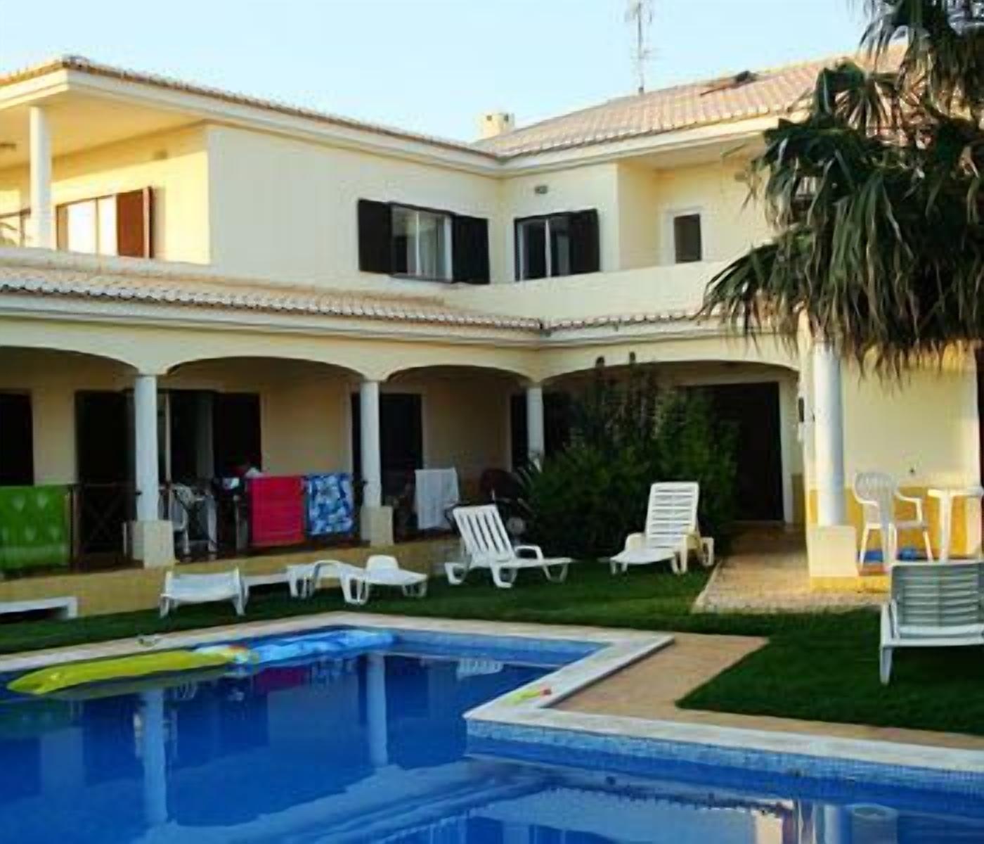 A two-story building with a swimming pool, outdoor seating, and a covered patio area.