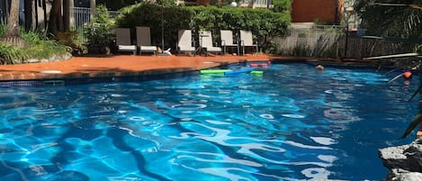 Una piscina al aire libre, sombrillas, sillones reclinables de piscina