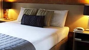 A hotel room with a brick wall, a bed with white bedding, two pillows, a bedside lamp, and a nightstand with a phone. - Shelly Beach Resort (Port Macquarie)