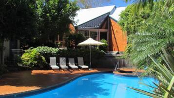 A swimming pool with lounge chairs and an umbrella.
