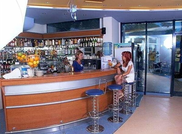 A bar area with a wooden counter, bar stools, and a variety of bottles and glasses. - Glarus (Nessebar)