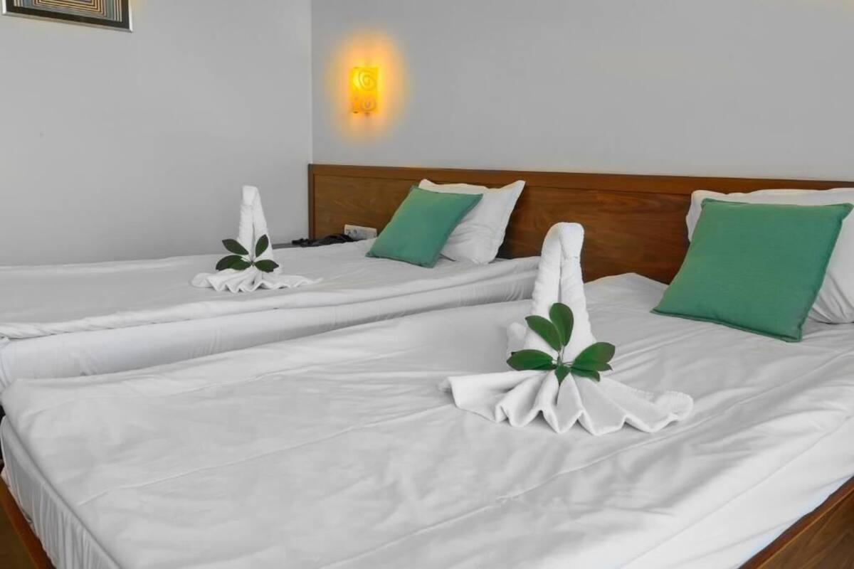 A hotel room with two beds, each with white linens and green pillows.