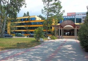 A hotel entrance with a covered walkway, a parking area, and a building with a sign reading "GLARUS". - Glarus (Nessebar)
