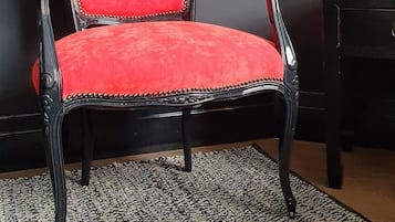 A chair with a red upholstered seat and black frame, placed on a patterned rug in a room with dark walls and a lamp.