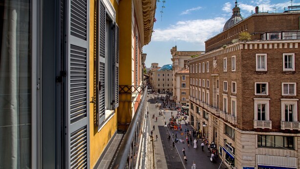 Vista da rua com edifícios, céu claro e uma cúpula distante.