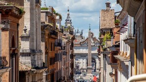 Uma rua estreita ladeada por edifícios históricos, com fachadas ornamentadas e um monumento imponente no centro.