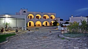 A courtyard with a building featuring multiple arches and a seating area with chairs and tables. - Masseria Tutosa (Ostuni)