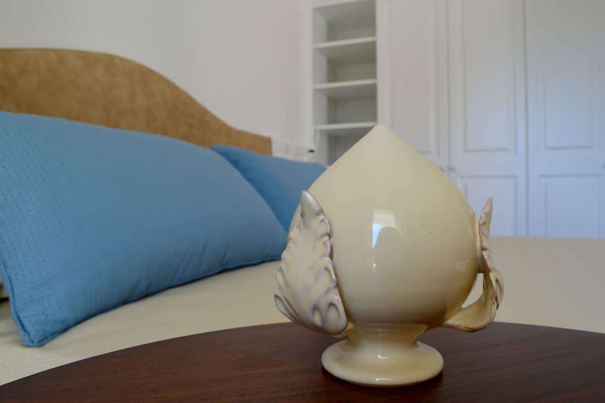 A white ceramic bowl with a floral pattern on a wooden table in a room with a bed and a blue pillow.