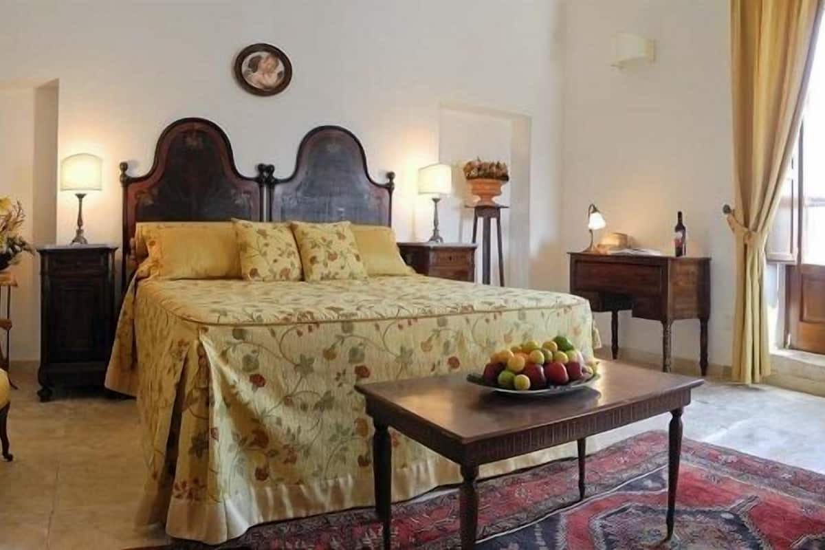 A bedroom with a bed, a chair, a table with fruit, and a lamp.