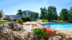 A pool area with lounge chairs, a clear blue pool, and a white building in the background. - Masseria Tutosa (Ostuni)