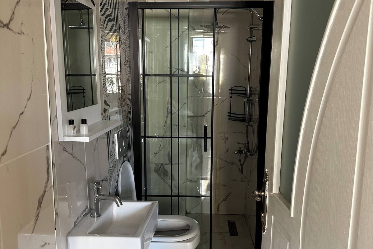 Un baño con lavamanos blanco, inodoro y cabina de ducha con mampara de vidrio.