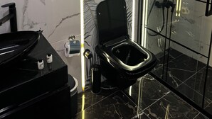 Un baño moderno con inodoro y tocador negros, y una ducha con mampara de vidrio.