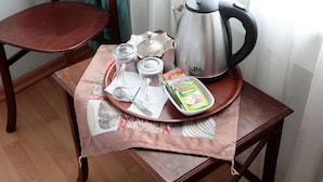 Una mesa de madera con una bandeja que contiene un hervidor de acero inoxidable, dos vasos, una cuchara, un tazón pequeño con sobres y una pañuelo.