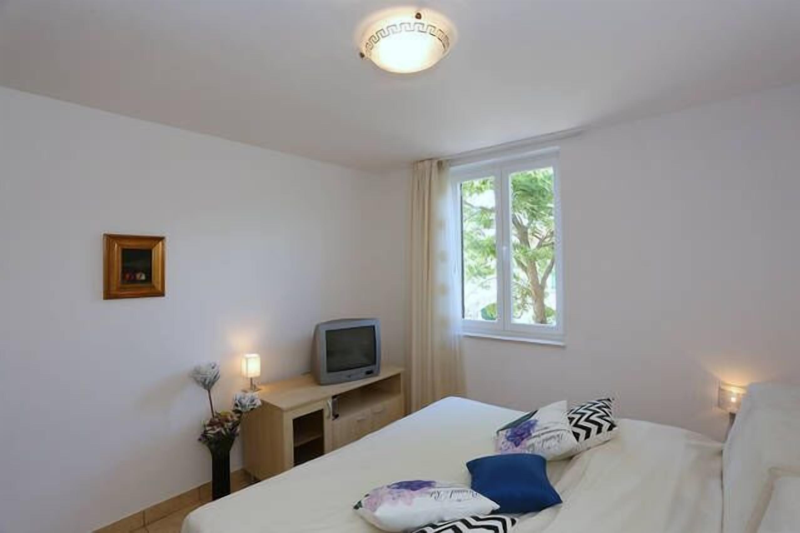 A hotel room with a bed, a television on a stand, a small desk, and a window with curtains.
