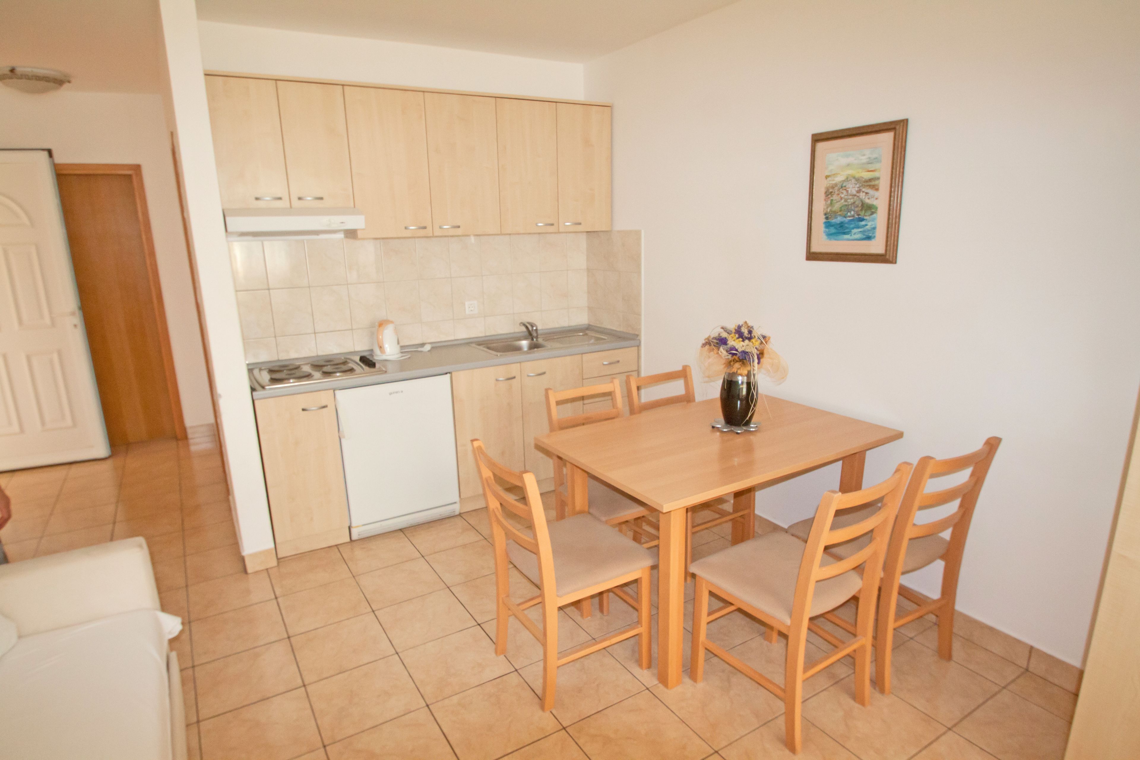 Una cocina compacta con armarios de madera, una encimera blanca y una mesa de comedor con sillas.