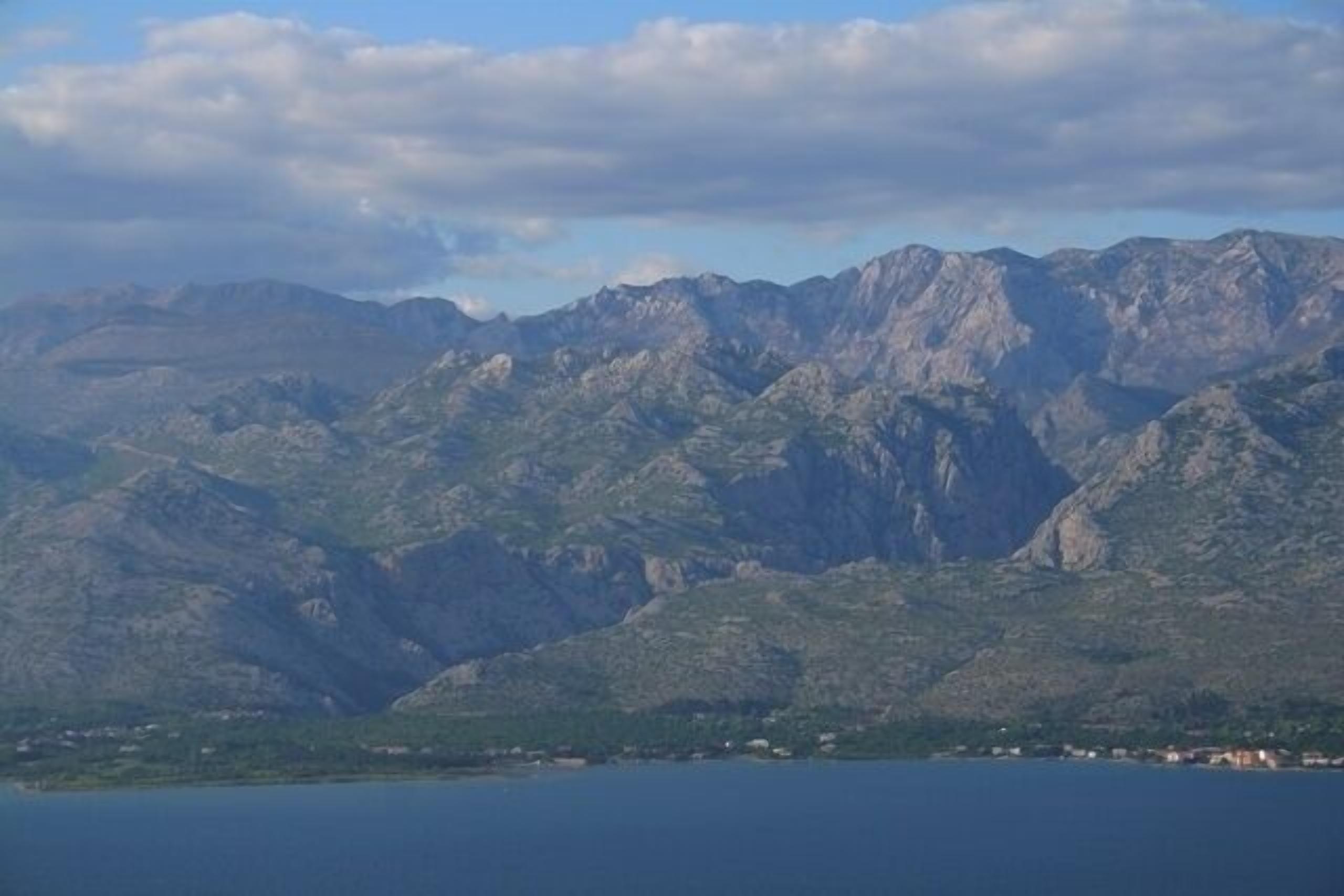 A mountainous landscape with a body of water in the foreground and a town at the base.