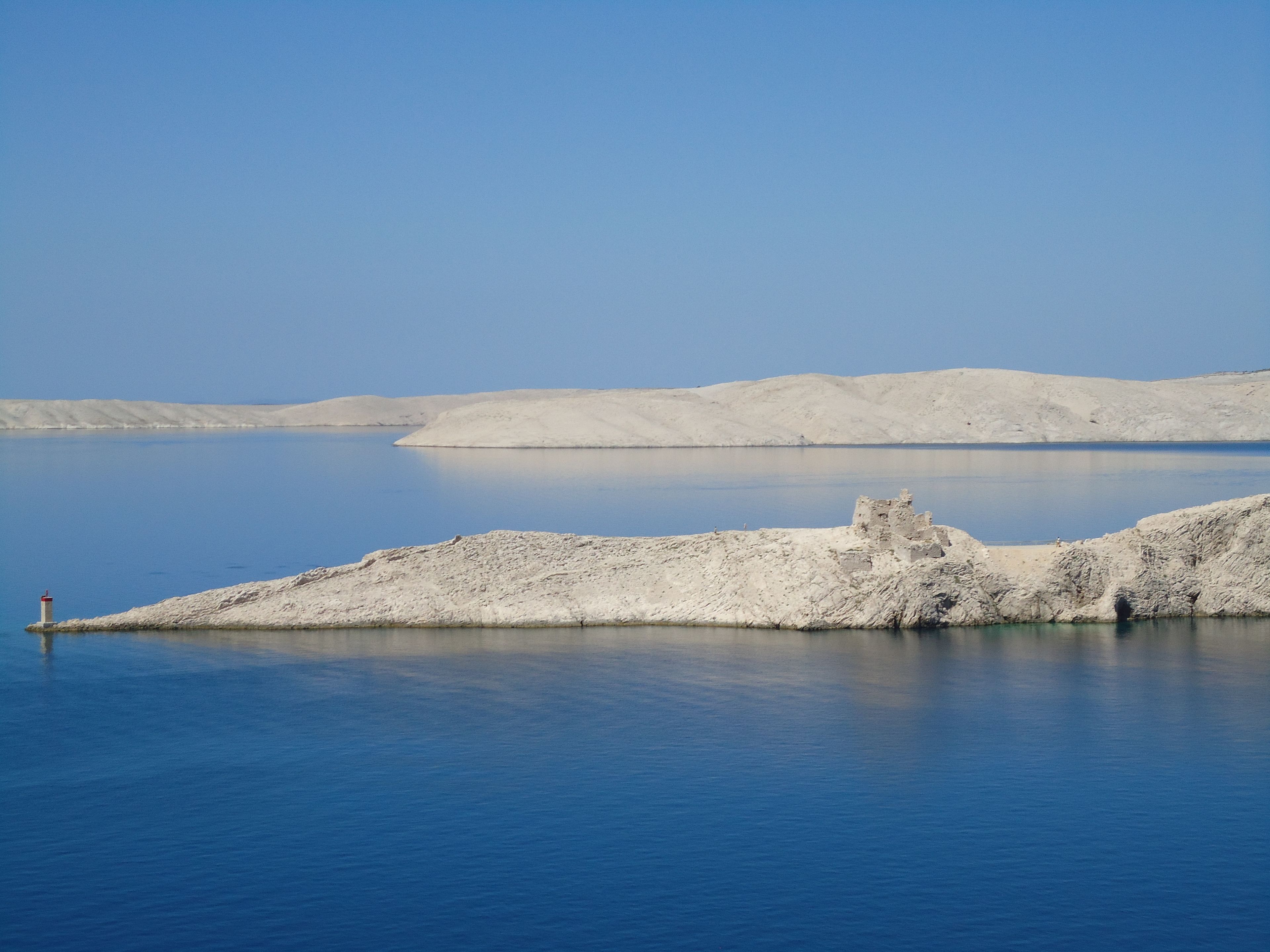 A calm lake with a rocky shoreline and a small structure in the distance.