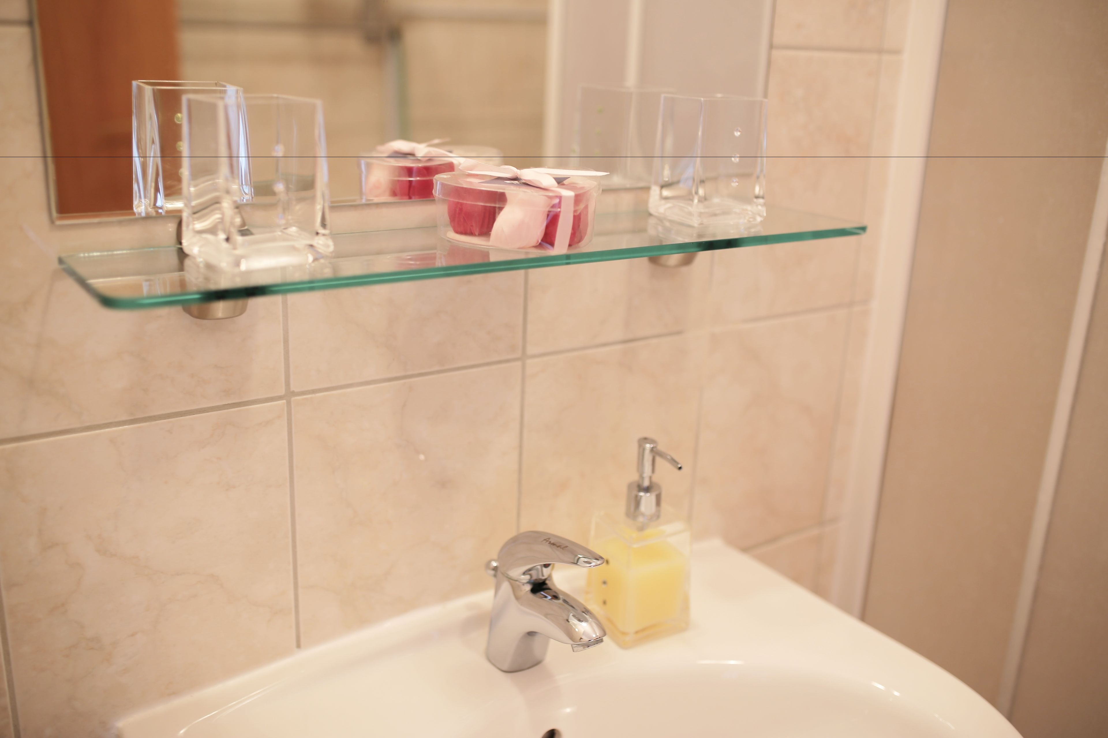 A bathroom with a glass shelf holding toiletries and a sink with a soap dispenser.