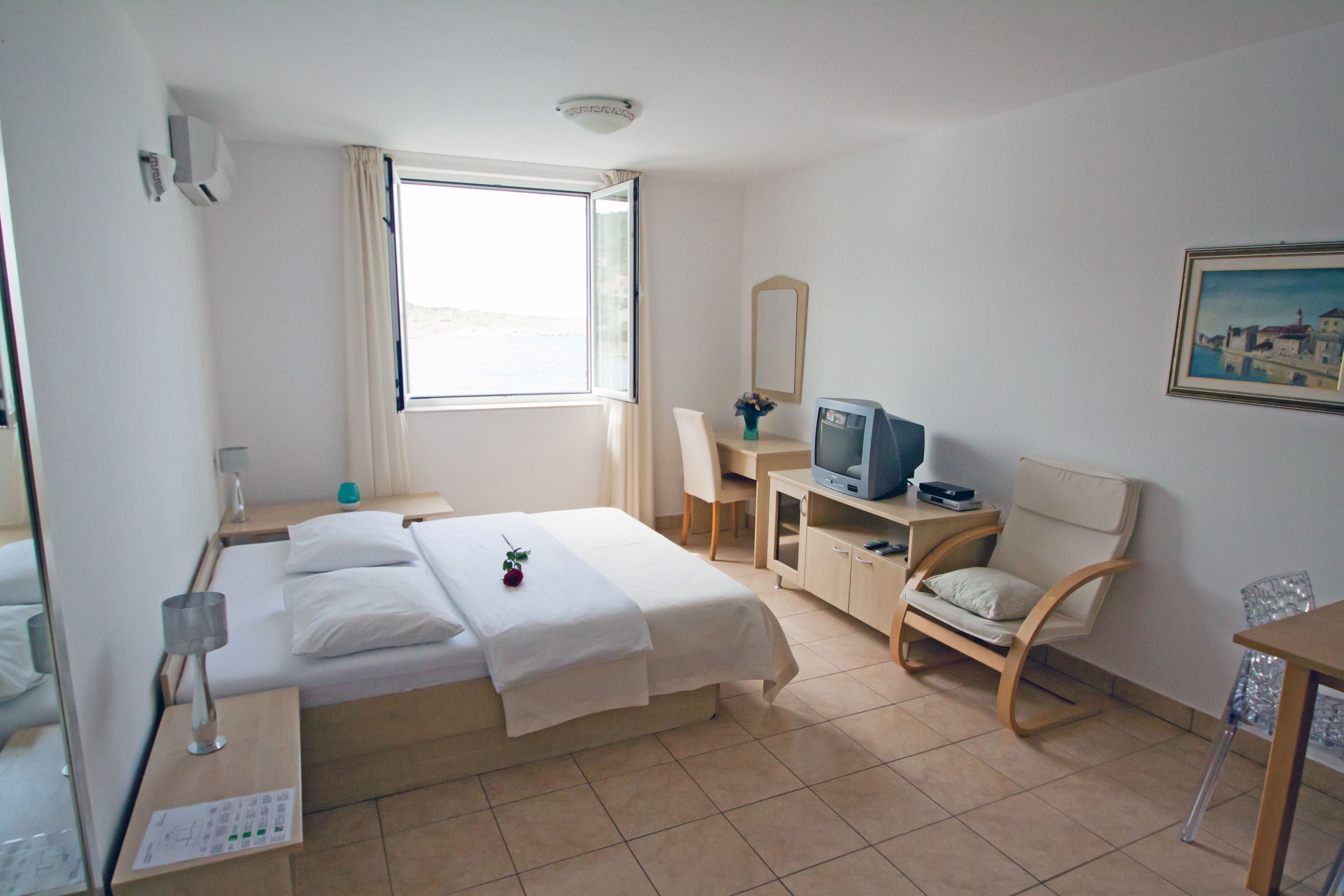 A hotel room with a bed, a desk with a computer, a chair, a TV, and a window with curtains.