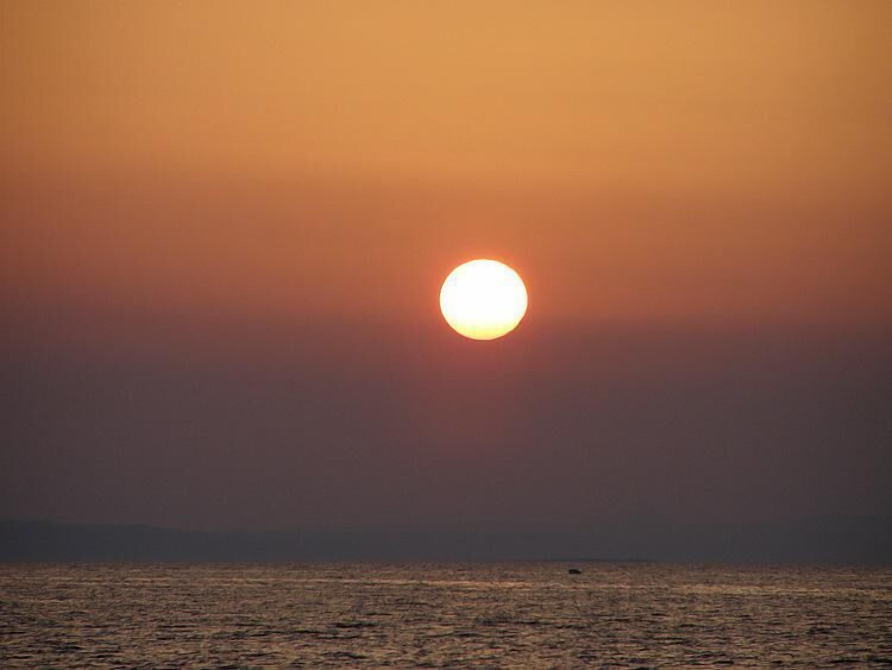 A sunset over a calm sea with a clear horizon.