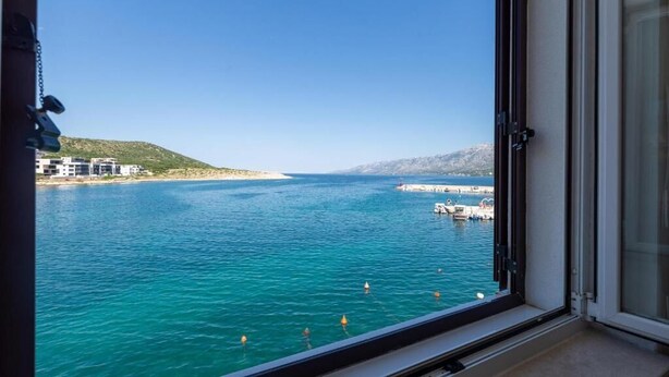 A view from a window overlooking a calm sea with a clear sky, a distant shoreline with buildings, and a small island with structures. - Tamarix Residence (Posedarje)