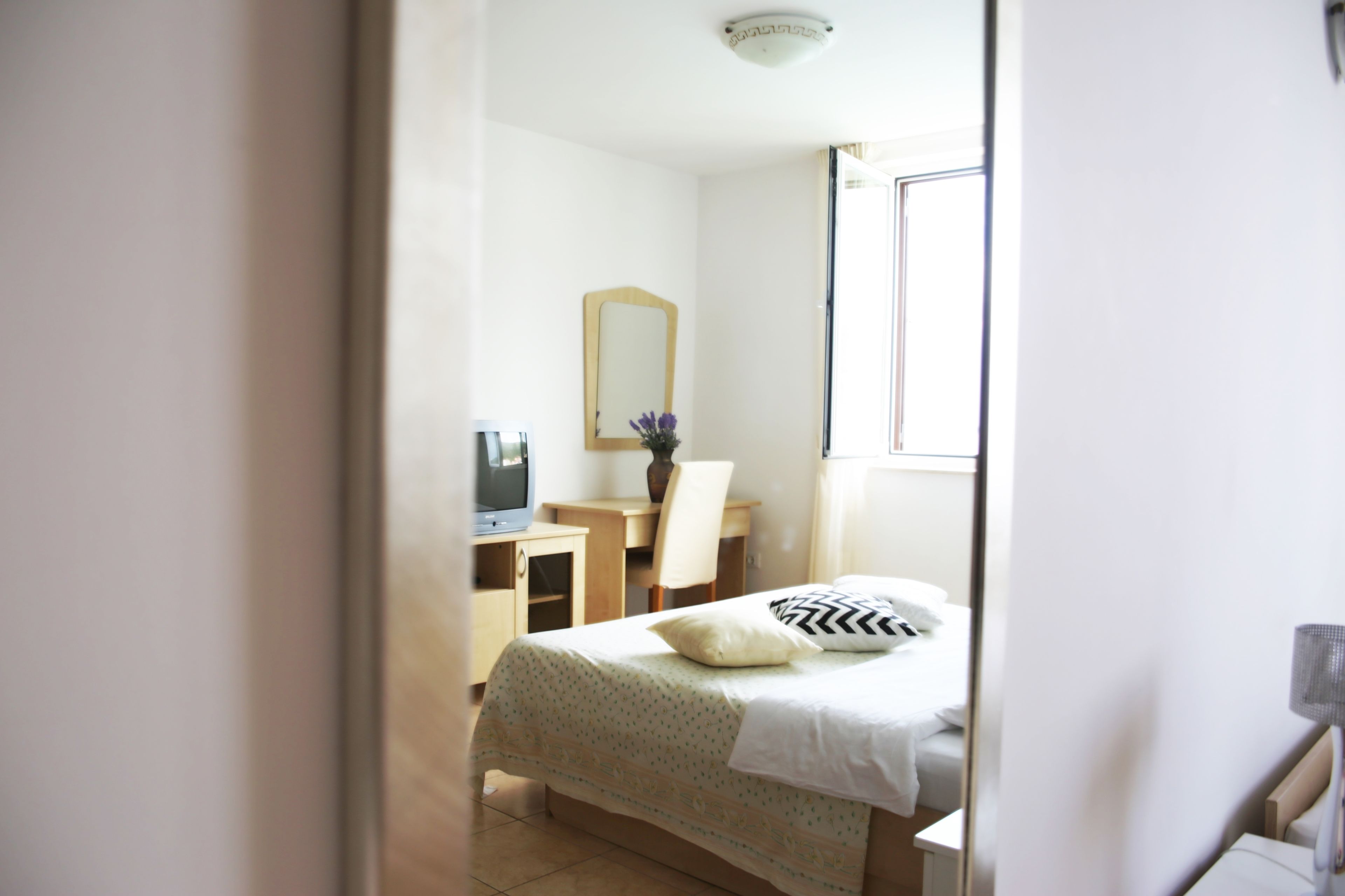 A bedroom with a bed, a desk, a chair, a television, and a mirror.
