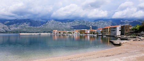 A coastal town with buildings along the waterfront, a calm lake, and mountains in the background.