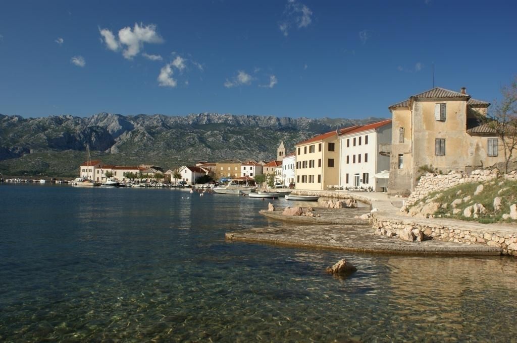 A coastal town with buildings along a clear waterfront, boats docked, and mountains in the background.