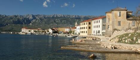 A coastal town with buildings along a clear waterfront, boats docked, and mountains in the background.