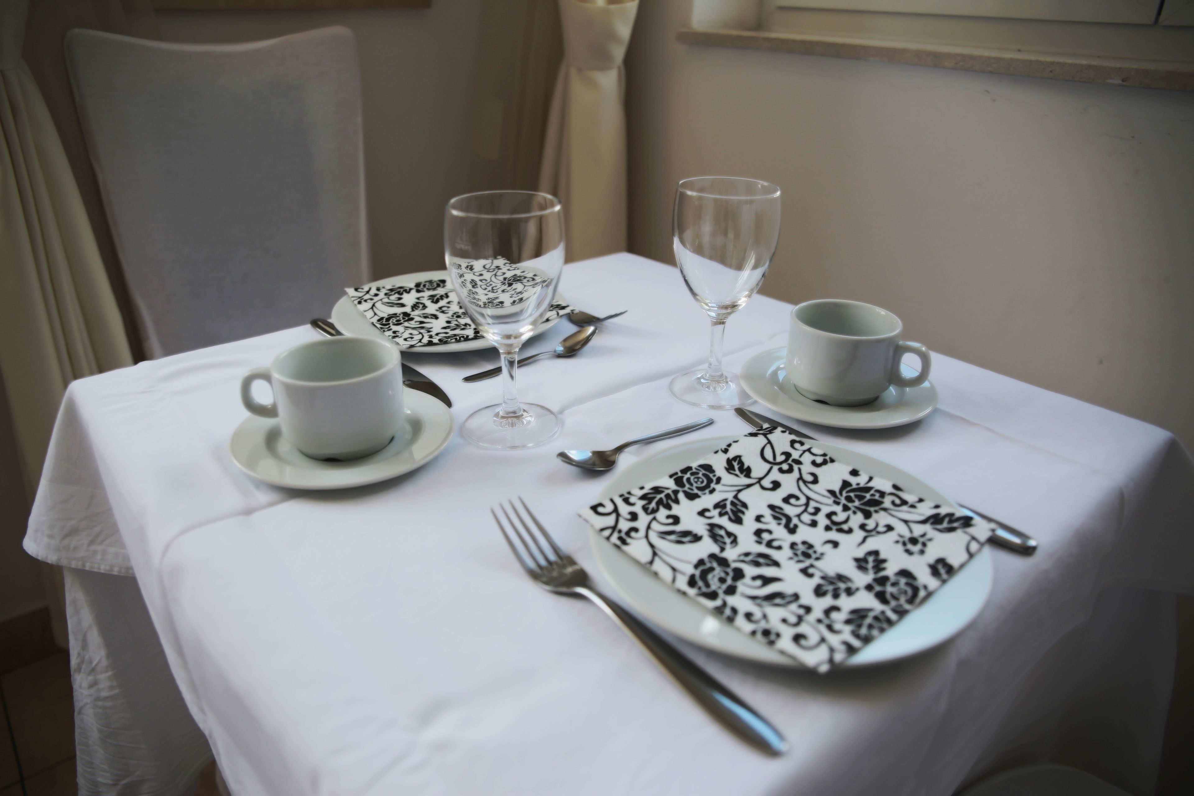 A table set for two with white tablecloth, black and white patterned plates, and clear glassware.