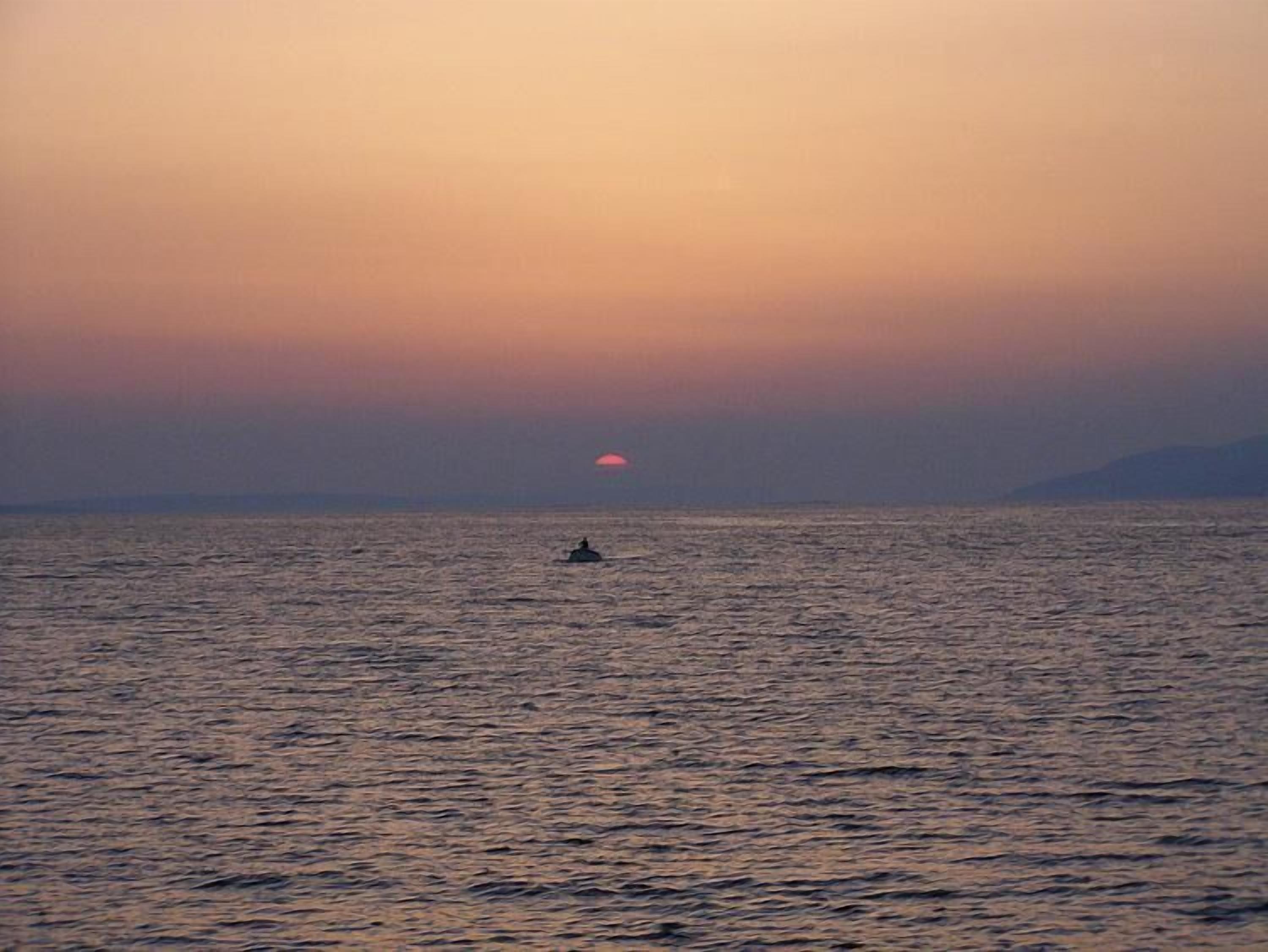 Ein Sonnenuntergang über einem ruhigen Meer, mit einem einzelnen Boot in der Ferne.