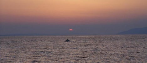 Solnedgang over et roligt hav med en enkelt båd i det fjerne.