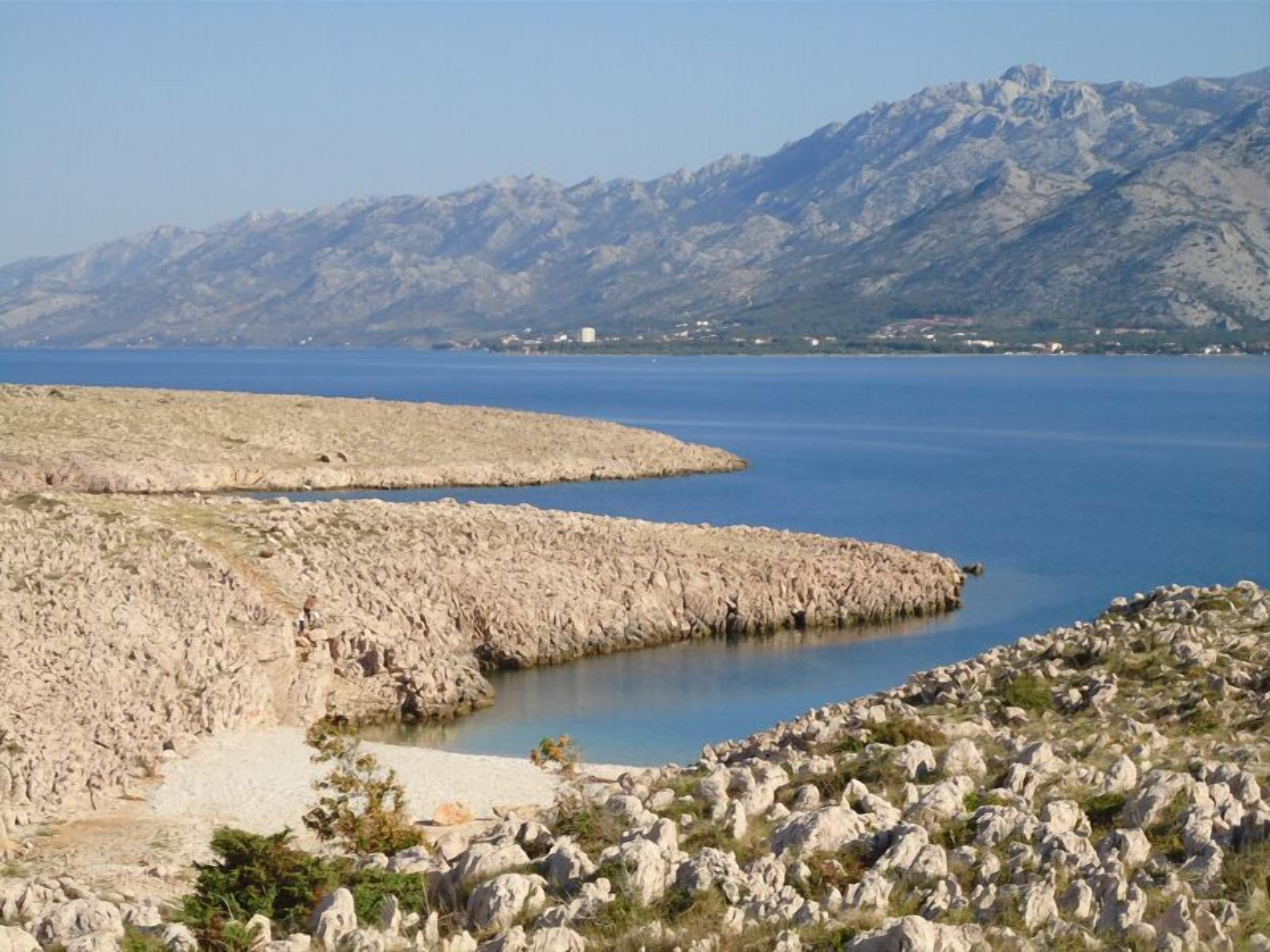 Un paysage côtier rocheux offrant une vue dégagée sur la mer et les montagnes lointaines.
