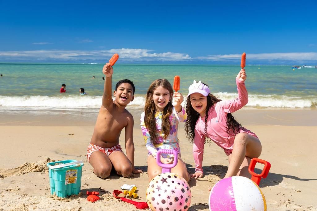 Cena de praia com crianças brincando, um balde azul e uma bola rosa com padrão de estrelas.