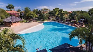 A large swimming pool with clear blue water, surrounded by palm trees and lounge chairs.
