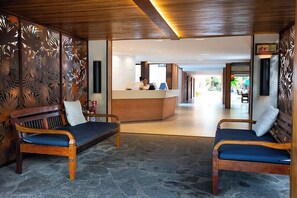 A reception area with a reception desk, two wooden benches with cushions, and a stone floor.