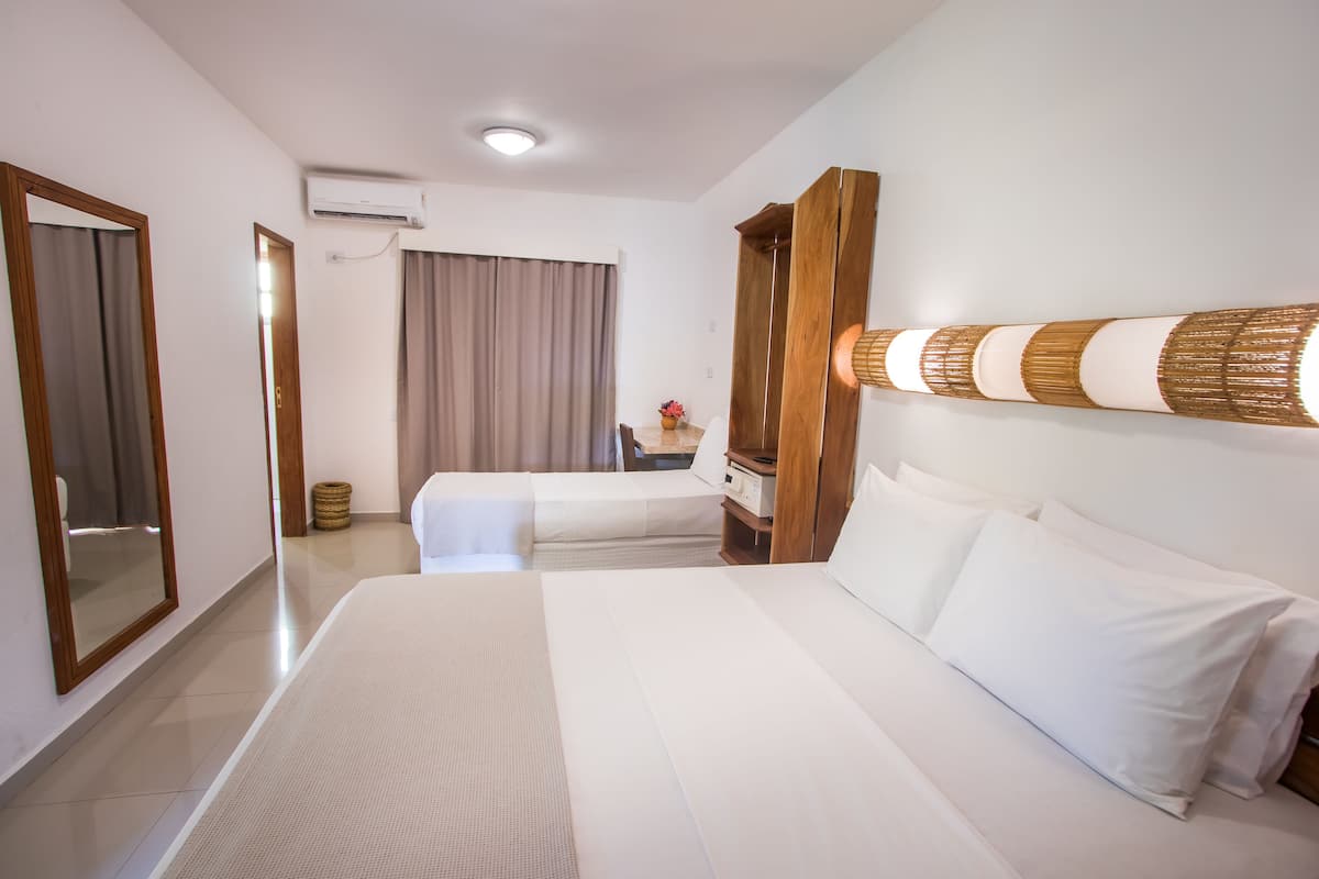 A hotel room with two beds, a large mirror, a wooden wardrobe, a wall-mounted lamp, and a ceiling air conditioner.