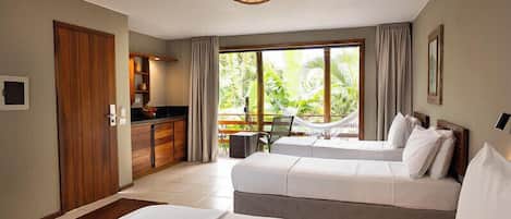 Habitación de hotel con dos camas, kitchenette y balcón con vista a zonas verdes.