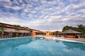 Una piscina amb gandules i ombrel·les, envoltada d'edificis d'estil arquitectònic tropical.