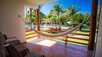 Una hamaca en un balcón con vista a la piscina, mobiliario de exterior y cielo despejado.