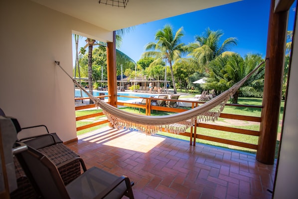 A hammock on a balcony with a pool view, outdoor seating, and a clear sky.